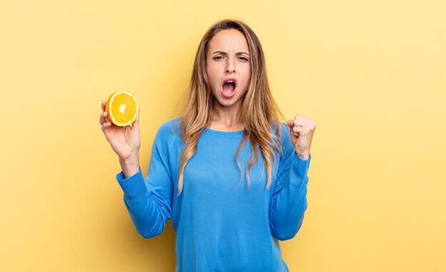 Mooie vrouw die agressief schreeuwt met een boze uitdrukking die half oranje vasthoudt