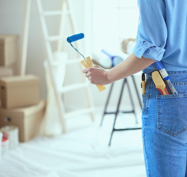 Mooie vrouw die binnenmuur van huis schildert met verfroller