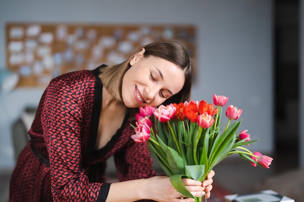 Mooie vrouw die bloemen schikt, gepresenteerd door haar man thuis, gelukkig en vreugdevol