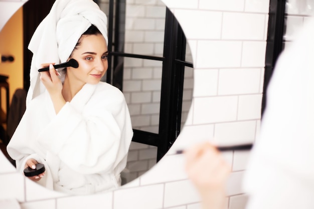 Mooie vrouw die borstel gebruikt voor dagelijkse make-up in de badkamer