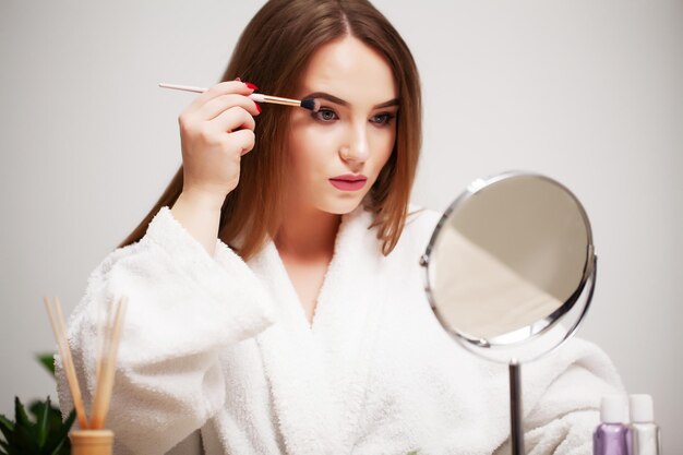 Mooie vrouw die borstel gebruikt voor dagelijkse make-up in de badkamer