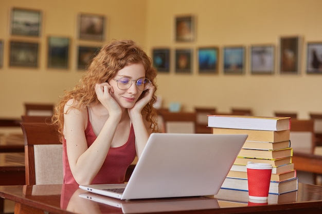 Mooie vrouw die de toevallige t-shirt van Bourgondië dragen en glazen die tekst via laptop lezen of noodzakelijke informatie zoeken