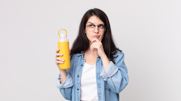 Mooie vrouw die denkt, zich twijfelachtig en verward voelt en een koffiethermoskan vasthoudt