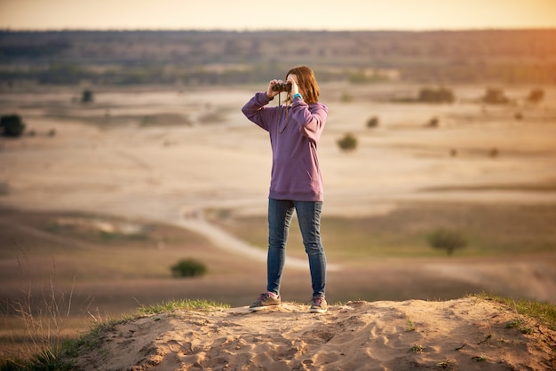 Mooie vrouw die door verrekijkers in openlucht zonsondergang bekijkt