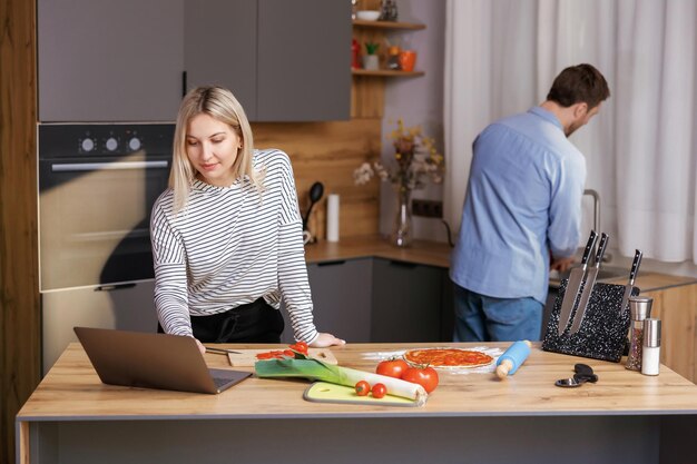 Mooie vrouw die een salade kookt in de keuken terwijl haar man erachter de afwas doet