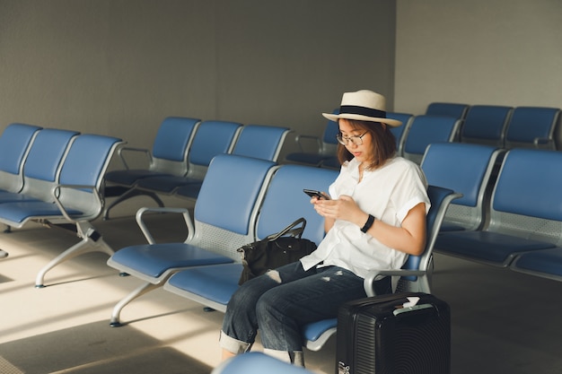 Mooie vrouw die een strohoed draagt die een slimme telefoon met behulp van Terwijl het zitten op het vliegtuig