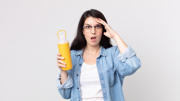 Mooie vrouw die er blij, verbaasd en verrast uitziet en een koffiethermoskan vasthoudt