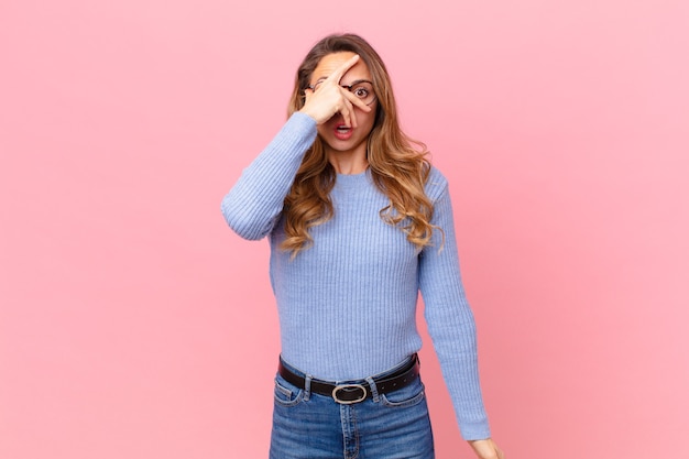 Mooie vrouw die geschokt, bang of doodsbang kijkt, haar gezicht bedekt met de hand