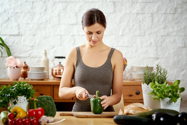 Mooie vrouw die groenten snijdt in de keuken.