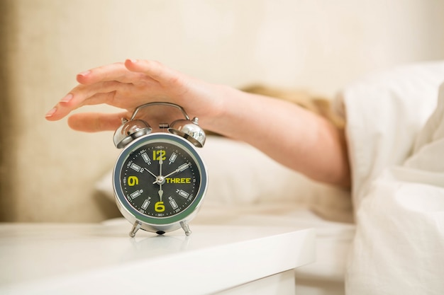 Mooie vrouw die haar wekker in de slaapkamer uitschakelt