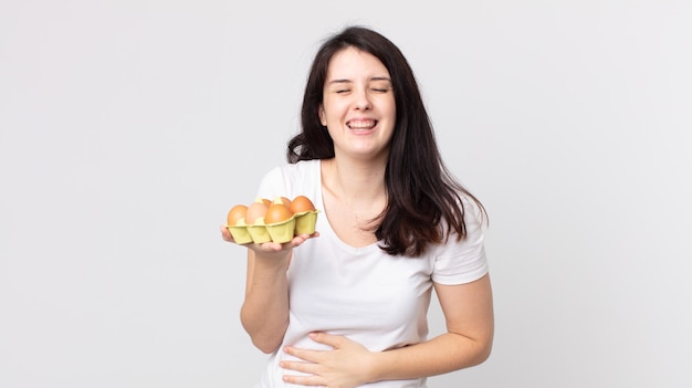 Mooie vrouw die hardop lacht om een hilarische grap en een eierdoos vasthoudt