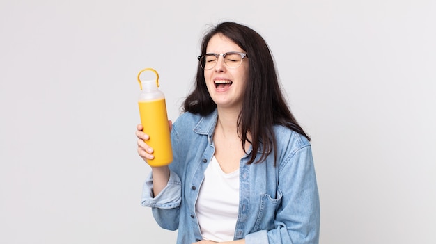 mooie vrouw die hardop lacht om een hilarische grap en een thermoskan koffie vasthoudt