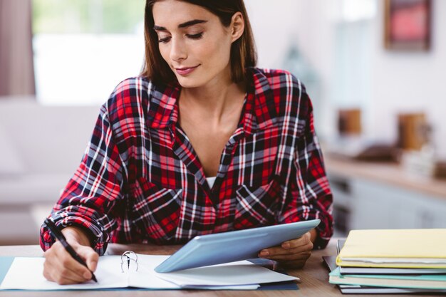 Mooie vrouw die in blocnote schrijft terwijl het houden van digitale tablet