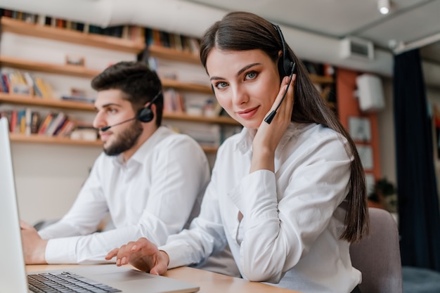 Mooie vrouw die in call centre met hoofdtelefoon en man werkt