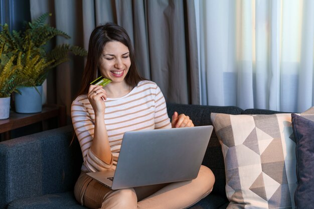 Mooie vrouw die in de woonkamer zit en online winkelt met creditcard, handig betalen met dig