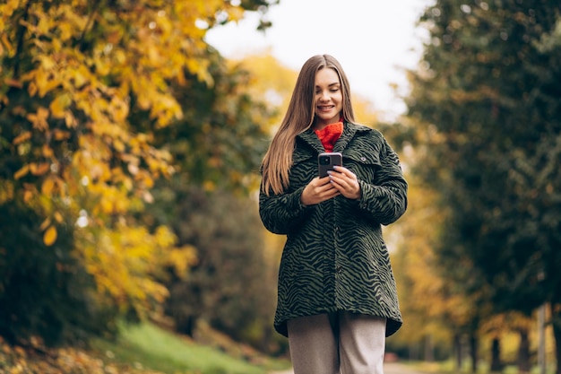 Mooie vrouw die in het herfstpark loopt en telefoon gebruikt