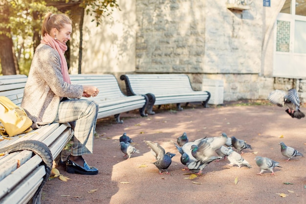 Mooie vrouw die in het park rust en duiven voert