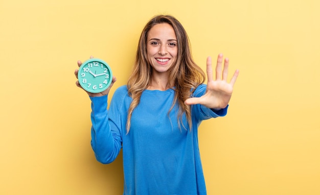 Mooie vrouw die lacht en er vriendelijk uitziet en nummer vijf toont met een wekker