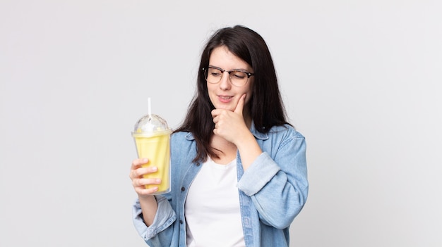 Mooie vrouw die lacht met een gelukkige, zelfverzekerde uitdrukking met de hand op de kin en een vanillemilkshake vasthoudt