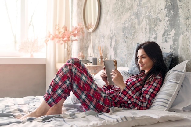 Mooie vrouw die lezingsboek in bed genieten van