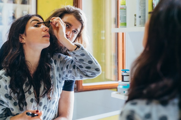 Mooie vrouw die mascara zet die door haar vriend wordt gekoesterd