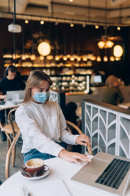 Mooie vrouw die medisch gezichtsmasker draagt die laptop gebruikt om te werken