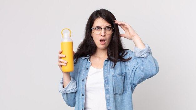 Mooie vrouw die met handen in de lucht schreeuwt en een koffiethermoskan vasthoudt