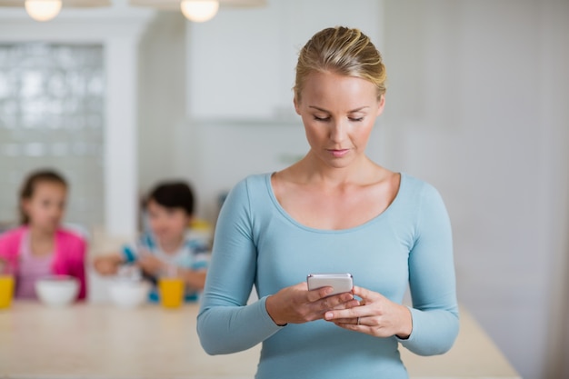 Mooie vrouw die mobiele telefoon in keuken met behulp van