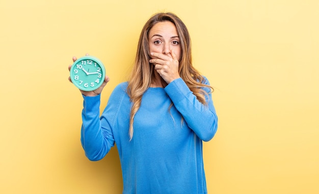 Mooie vrouw die mond bedekt met handen met een geschokte met een wekker