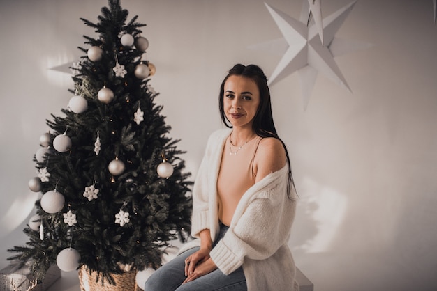 Mooie vrouw die Nieuwjaar en Kerstmis viert bij versierde kerstboom en slingers