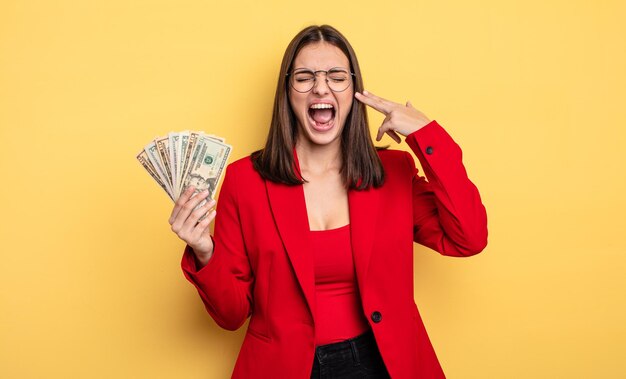 Mooie vrouw die ongelukkig en gestrest zelfmoordgebaar kijkt en een pistoolteken maakt met dollarbankbiljettenconcept