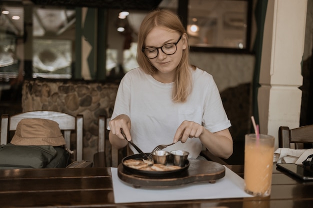 Foto mooie vrouw die ontbijt met sapdrank eet met smartphone die bij restaurant zit. gezond ontbijt