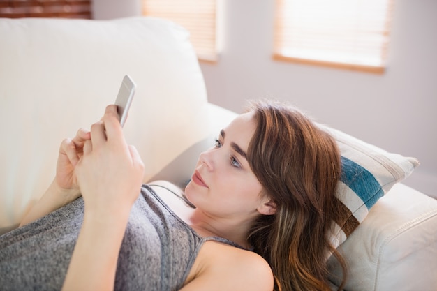 Mooie vrouw die op de laag ligt die telefoon in de woonkamer met behulp van