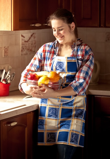 Mooie vrouw die schort draagt die verse kom met fruit houdt