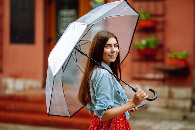 Mooie vrouw die smartphone op straat gebruikt bij regenachtig weer glimlachend met paraplu Zomerregen