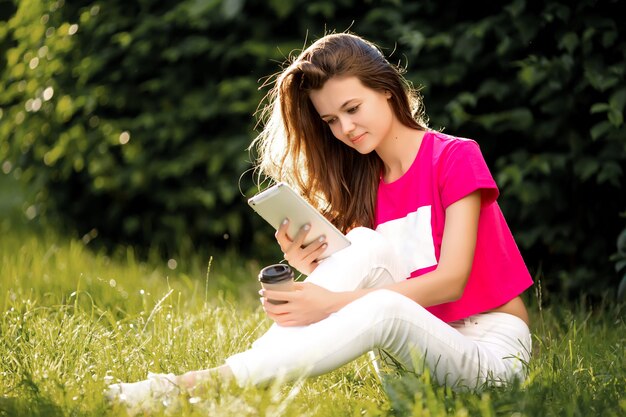 Foto mooie vrouw die tablet gebruiken terwijl het zitten op gras in het groene park