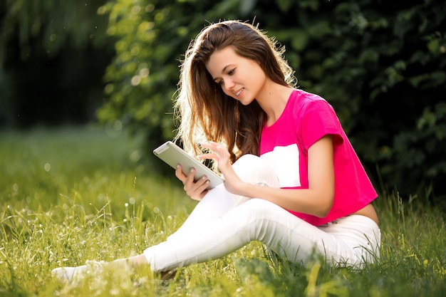 Foto mooie vrouw die tablet gebruiken terwijl het zitten op gras in het groene park