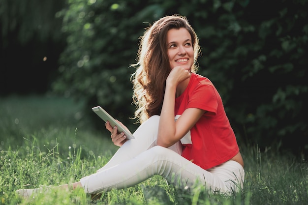 Mooie vrouw die tablet gebruiken terwijl het zitten op gras in het park