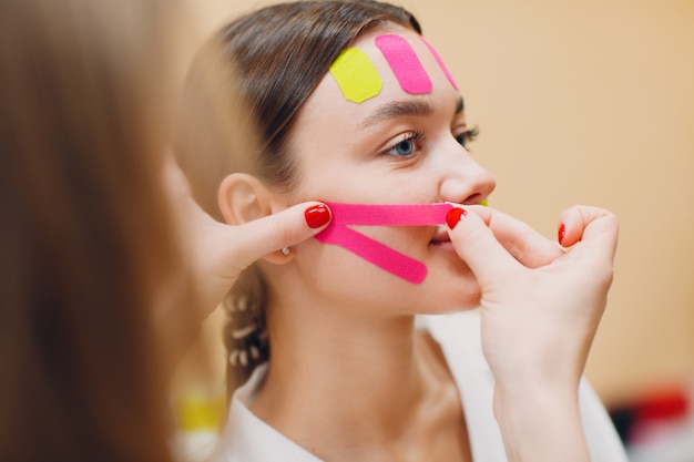 Mooie vrouw die tape opheffende behandeling op het gezicht toepast