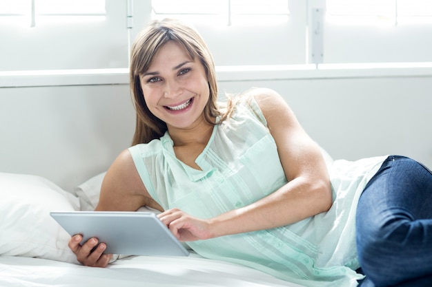 Mooie vrouw die terwijl het gebruiken van digitale tablet op bed glimlacht