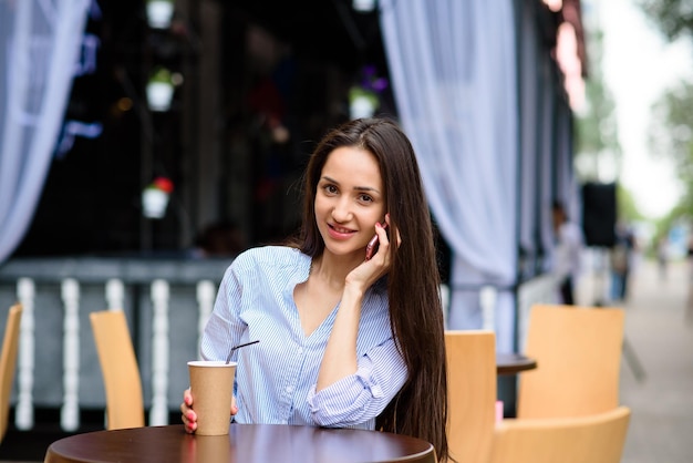 Mooie vrouw die thee drinkt en telefonisch praat in straatcafé