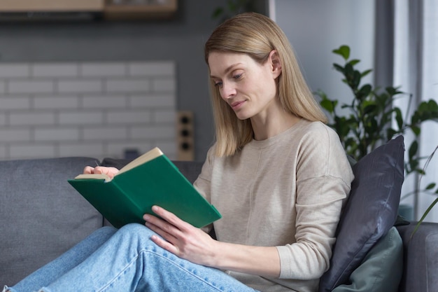 Mooie vrouw die thuis ontspant na het werk en een interessant boek leest dat op de bank zit