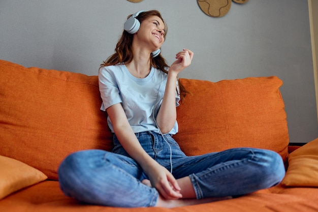 Mooie vrouw die thuis op de bank zit en naar muziek luistert op hoofdtelefoontechnologieën