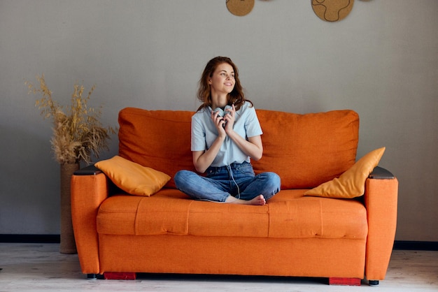 mooie vrouw die thuis op de bank zit en naar muziek luistert op koptelefoon appartementen foto van hoge kwaliteit