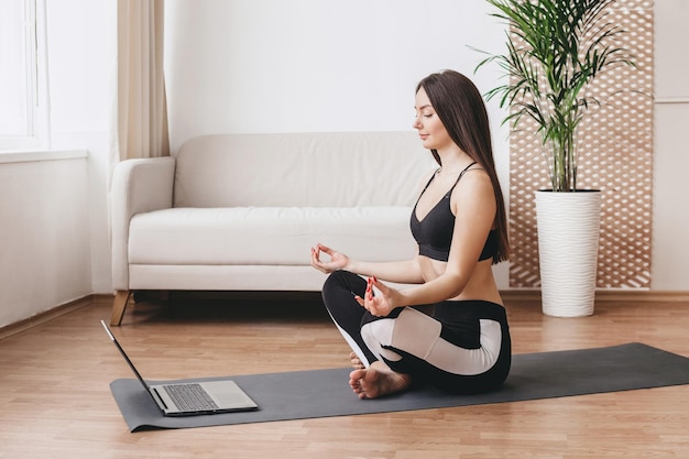 Mooie vrouw die thuis yoga doet en op een zonnige dag naar een zelfstudieles op laptop kijkt