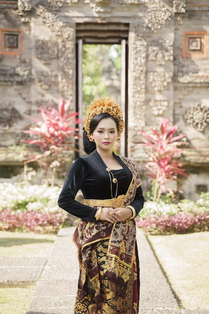 Mooie vrouw die traditionele Balinese kleren draagt die staan