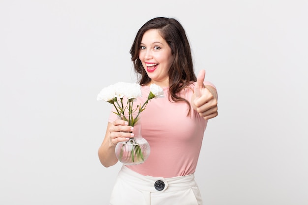 Mooie vrouw die trots is, positief glimlacht met duimen omhoog en een decoratieve bloemenpot vasthoudt