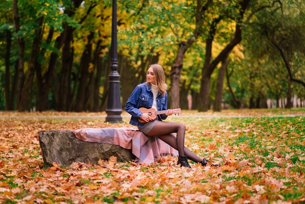 Mooie vrouw die ukelele gitaar speelt in de buitenlucht in een herfstbos