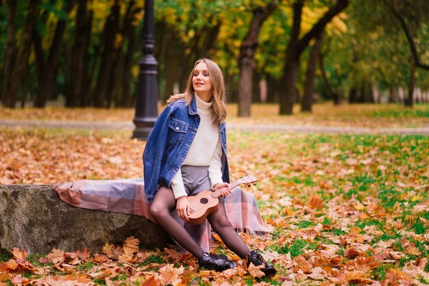 Mooie vrouw die ukelele-gitaar speelt in de buitenlucht in het herfstbos