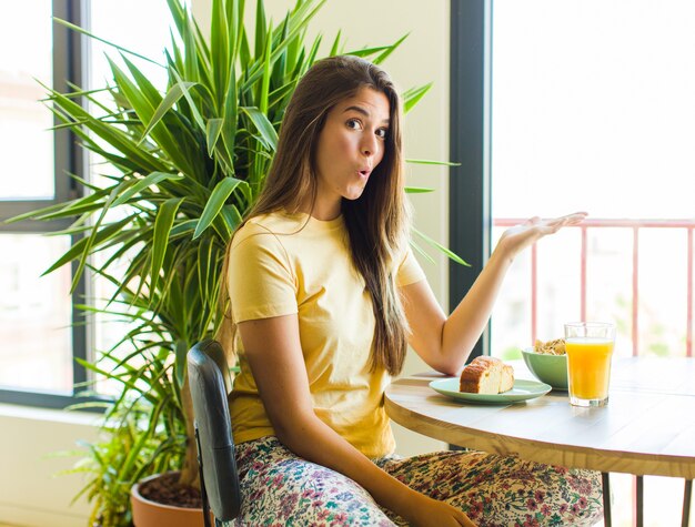 Mooie vrouw die verbaasd en geschokt kijkt, met open mond een voorwerp met een open hand opzij